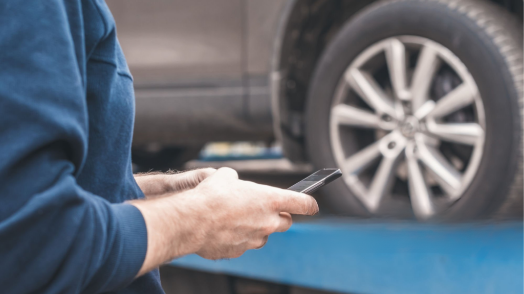 A photo of a man checking his phone for information while his car is being towed in the background.